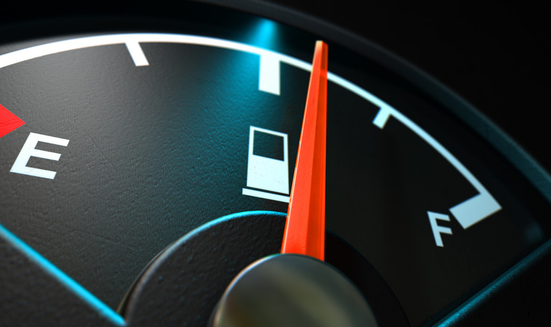 A closeup of a backlit illuminated gas gage with the needle indicating a half full tank on an isolated dark background